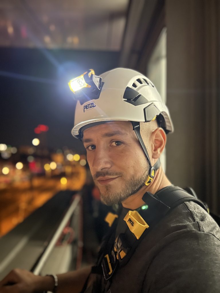 Höhenarbeiter mit Petzl Aria 2R Stirnlampe am Helm bei Nacht in der Stadt