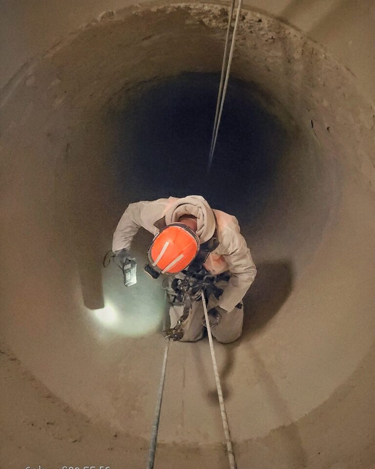 Industriekletterer seilt sich im Schutzanzug in einen Schacht ab